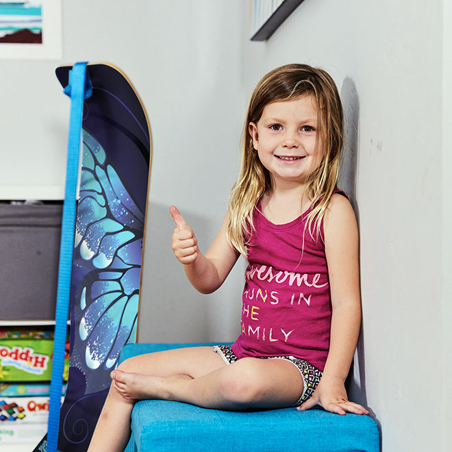 Young girl sitting on a blue chair with a Butterfly SlackBoard leaning against a wall.