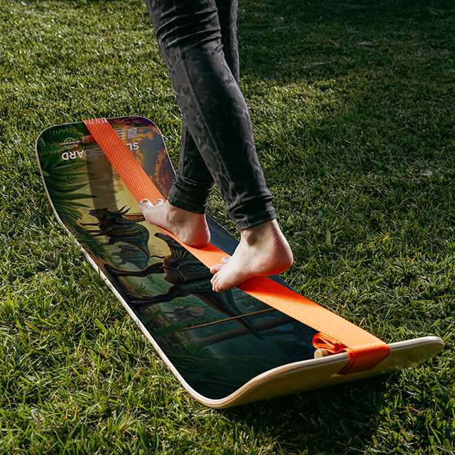 Person standing on a GIBBON Dino SlackBoard with orange line on grass
