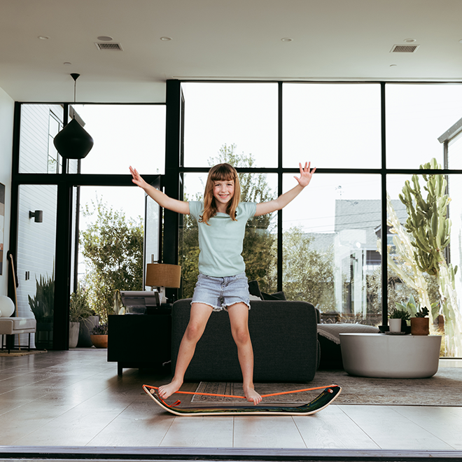 Child standing on a slackboardnin a modern living room with large windows.