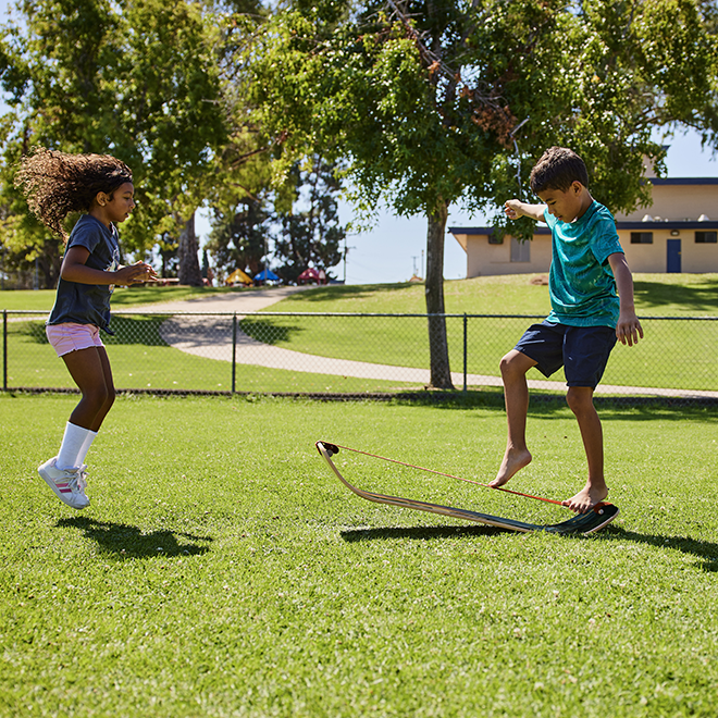 Two children playing with a slackboard in a park on a sunny day.
