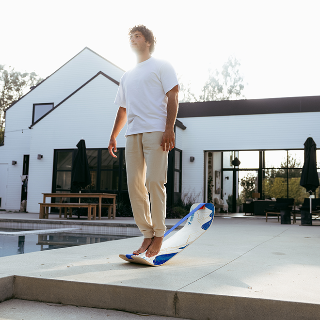 Person standing on a blue and white mountain slackboard in front of a modern house.